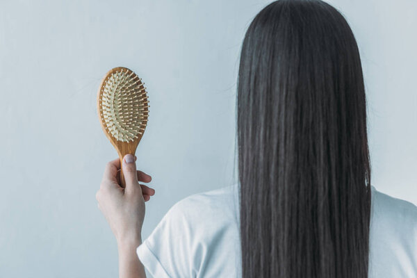back view of brunette woman holding hairbrush with fallen hair isolated on grey