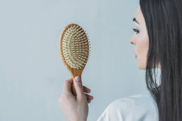 cropped shot of brunette woman holding hairbrush with fallen hair isolated on grey