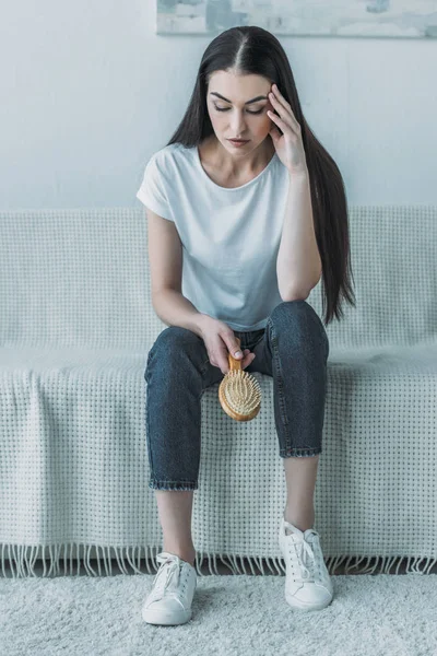 伤心的年轻女子拿着梳子坐在沙发上脱发概念 — 图库照片