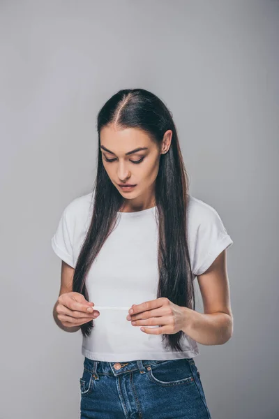 frustrated young woman holding pregnancy test isolated on grey