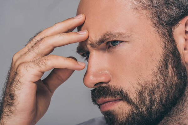 close-up view of sad bearded man with hand on forehead looking away isolated on grey