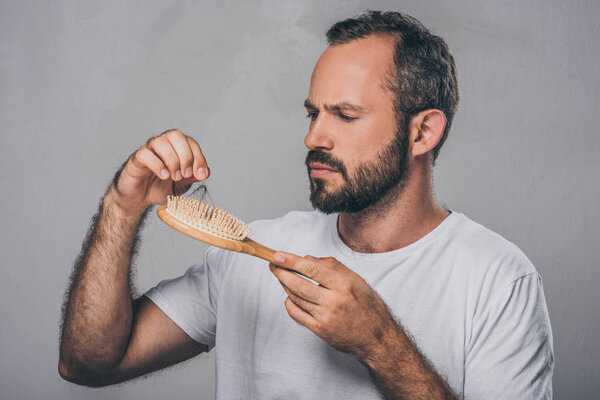 bearded middle aged man holding hairbrush, hair loss concept