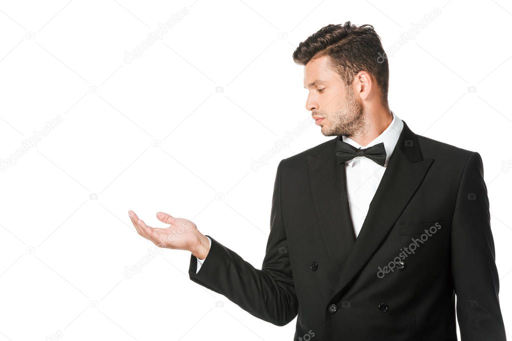 serious young man in suit looking at empty hand isolated on white