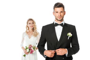 yakışıklı genç damat ceket kadar düğmelerini ve arka plan üzerinde beyaz izole üzerinde bulanık duran gelin kameraya bakarak