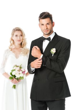 kol düğmesi kadar düğmelerini ve arka plan üzerinde beyaz izole üzerinde bulanık duran gelin kameraya bakarak yakışıklı genç damat