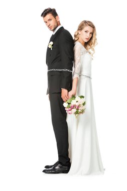ciddi genç newlyweds sırt sırta zincirle bağladılar ve kameraya bakarak beyaz izole