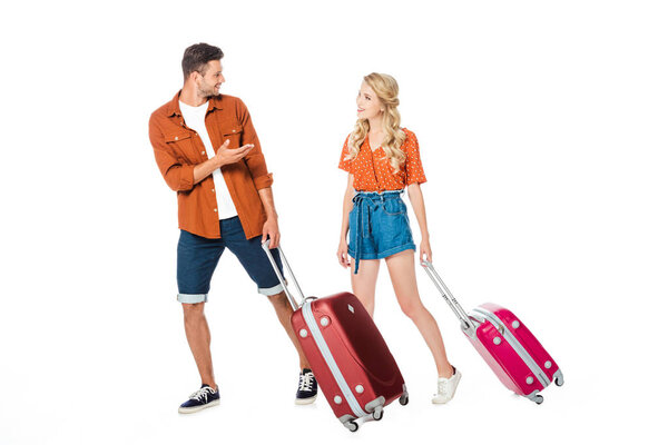 happy young couple with luggage walking and chatting isolated on white