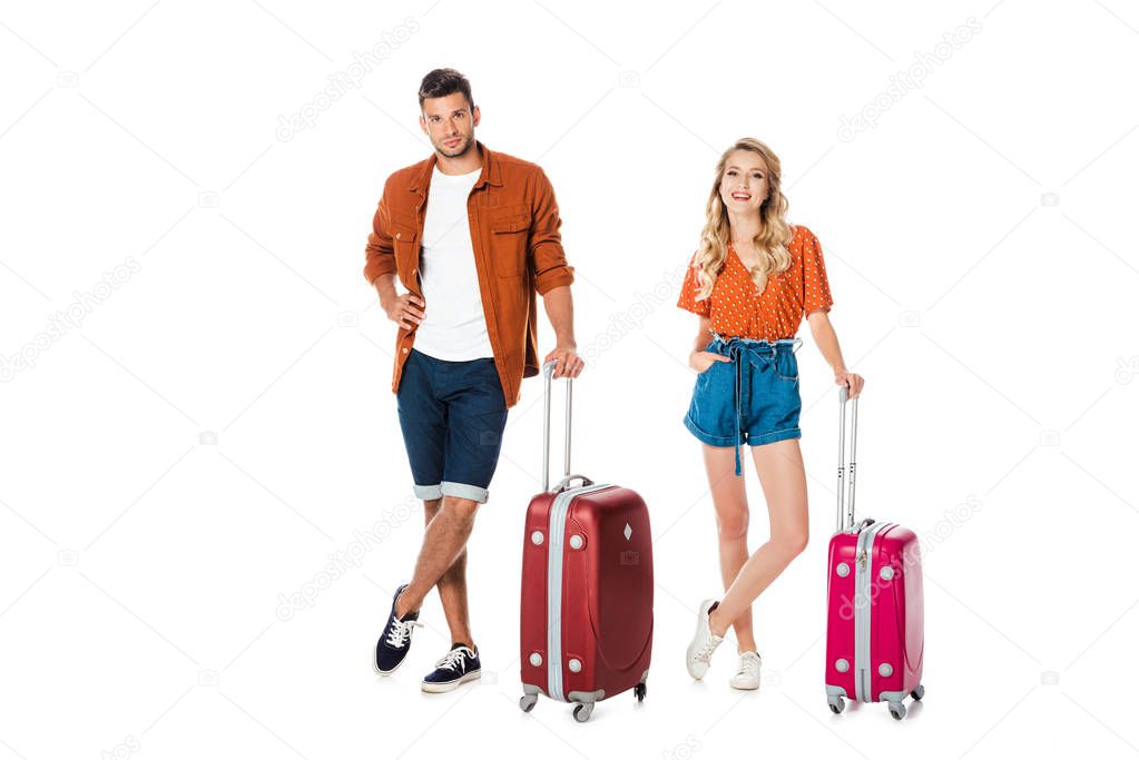 attractive young couple with suitcases looking at camera isolated on white