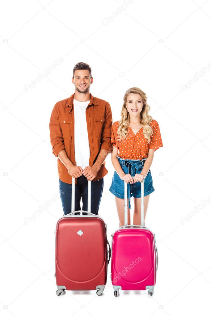 happy young couple with suitcases looking at camera isolated on white