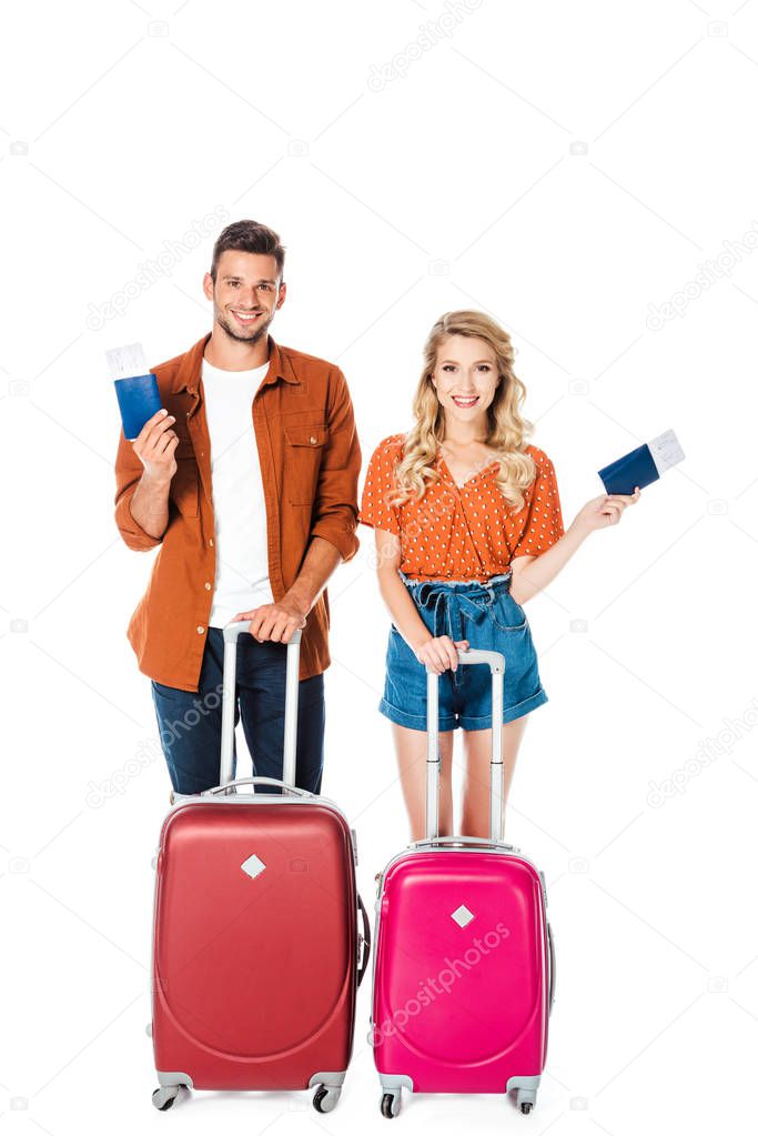 happy young couple with luggage and flight tickets looking at camera isolated on white