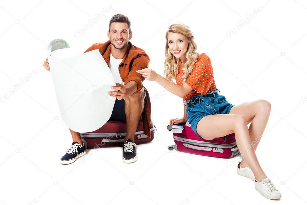 smiling couple sitting on travel bags with map isolated on white 