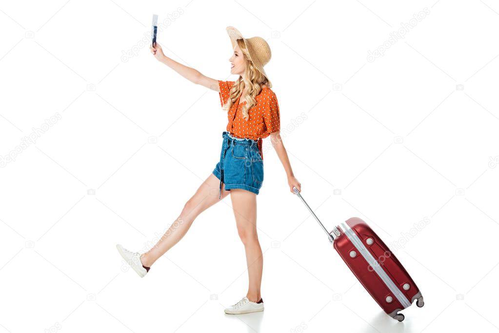 side view of beautiful girl walking with travel bag, passport and ticket isolated on white