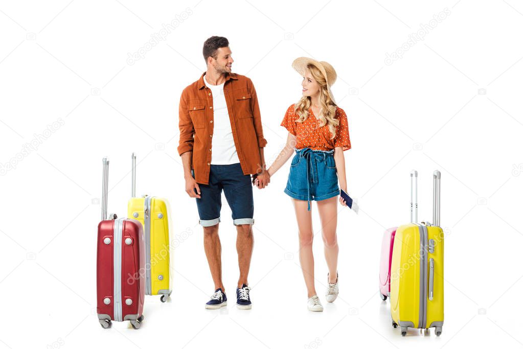 newlywed couple holding hands and looking at each other with suitcases around isolated on white