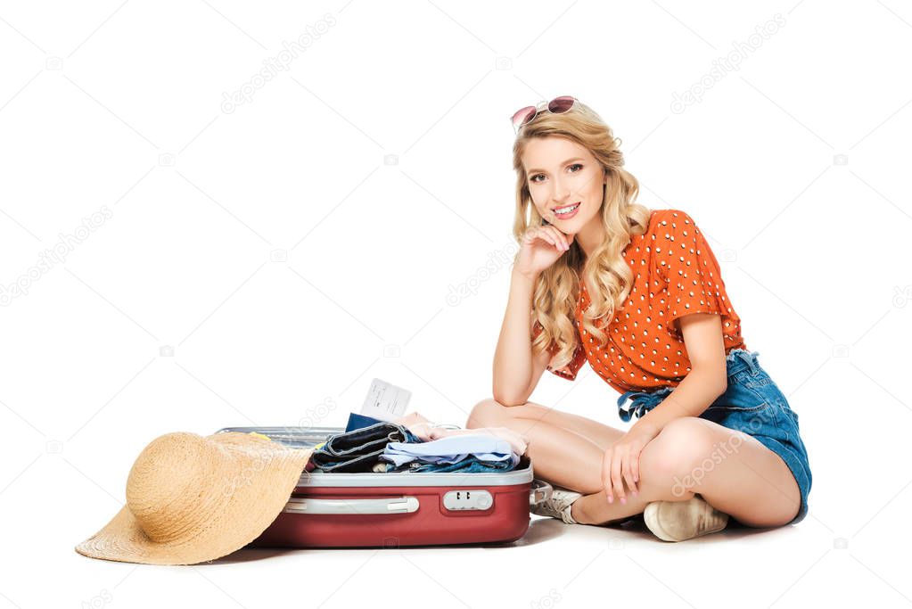 smiling young woman sitting at opened suitcase isolated on white