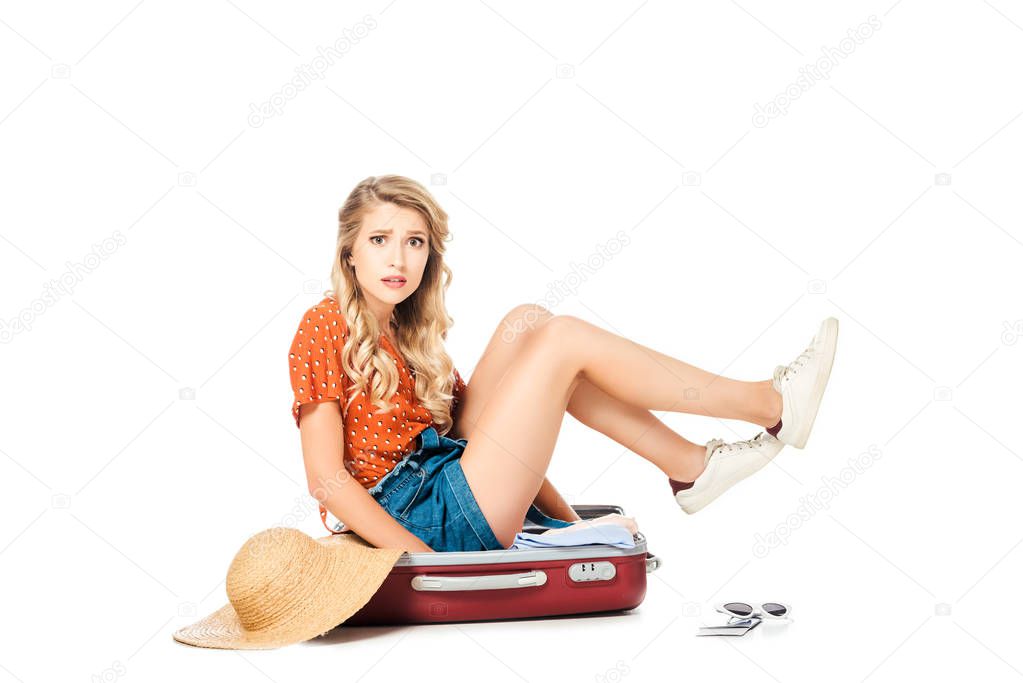 confused young woman trying to pack full suitcase isolated on white