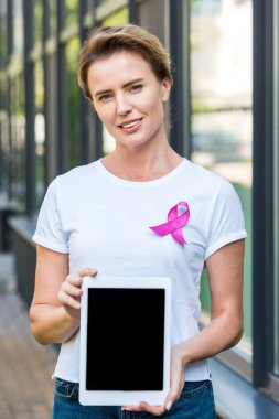 woman with pink ribbon holding digital tablet and looking at camera, breast cancer awareness concept     clipart