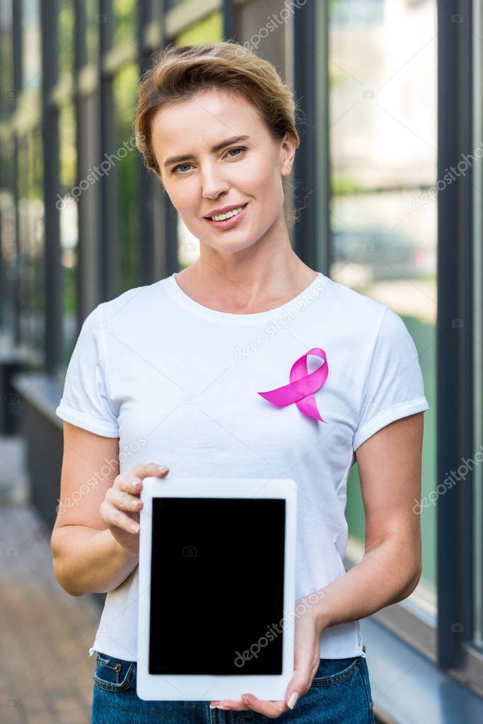 woman with pink ribbon holding digital tablet and looking at camera, breast cancer awareness concept    