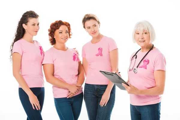 女性在粉红色 T恤与乳腺癌意识丝带看着微笑的资深医生与听诊器和剪贴板在白色隔离 — 免费的图库照片