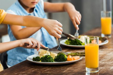 cropped shot of children eating healthy vegetables at wooden table clipart