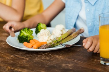 Çocuk sağlıklı sebze yemek yerken çatal ve bıçak tutarak kısmi görmek