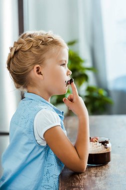 side view of cute little child eating delicious chocolate spread and looking away clipart
