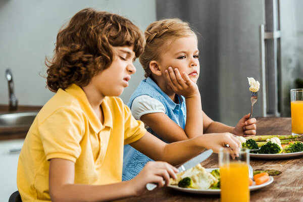 side view of unhappy little kids eating vegetables 