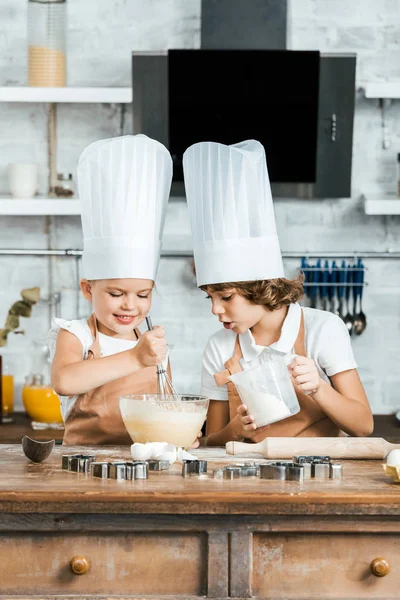 Niedlich Lächelnde Kinder Schürzen Und Kochmützen Bereiten Gemeinsam Teig Für — Stockfoto