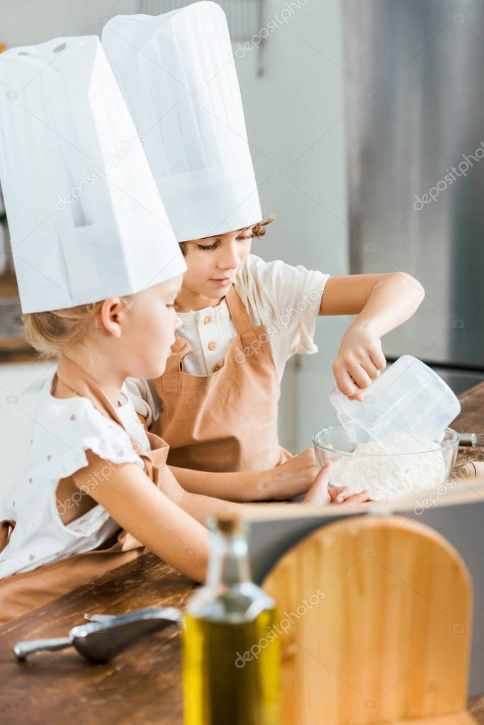 cute little children in chef hats preparing dough for cookies in kitchen  