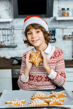 lezzetli zencefilli kurabiye tutarak ve kameraya gülümseyen santa şapkalı şirin mutlu çocuk