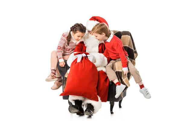 santa showing whats inside his sack to kids while they sitting in armchair together isolated on white