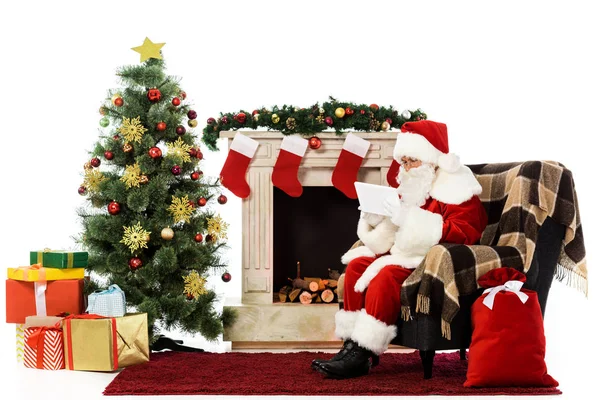 圣诞老人使用片剂 而坐在扶手椅附近的壁炉在白色隔离 — 图库照片