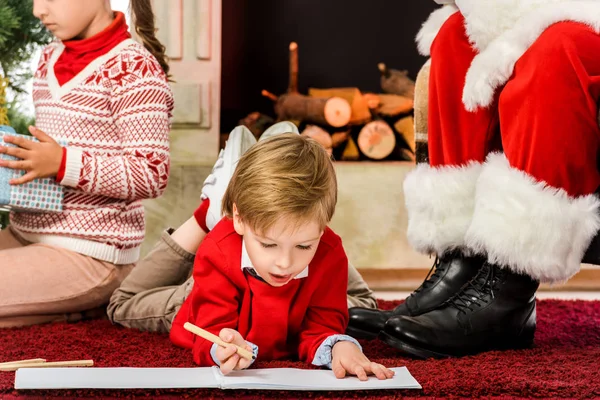 孩子们在圣诞老人附近的地板上打开礼物和画画的镜头 — 图库照片