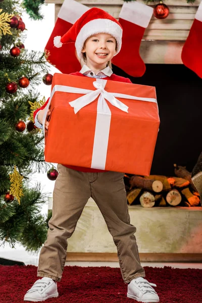 Smiling Little Kid Holding Big Red Christmas Gift Looking Camera — Free Stock Photo