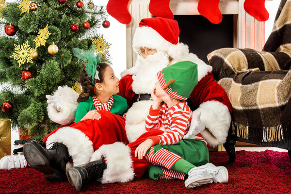 santa embracing kids while they sitting on floor in front of fireplace together