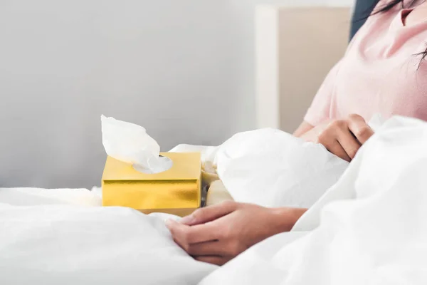 ベッドに座って紙ナプキンのボックスで病気の女性のショットをトリミング — ストック写真