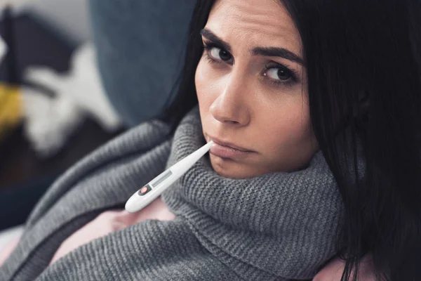 Kranke Junge Frau Misst Temperatur Mit Mundthermometer Und Blickt Kamera — kostenloses Stockfoto