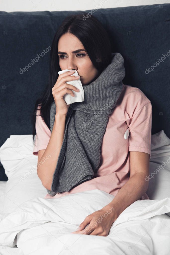 sick young woman covering mouth with napkin during cough in bed