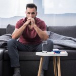Depressed young man sitting on couch and thinking with medicines on table