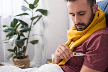 hasta genç adam yatakta elektronik termometre ile sıcaklık ölçme