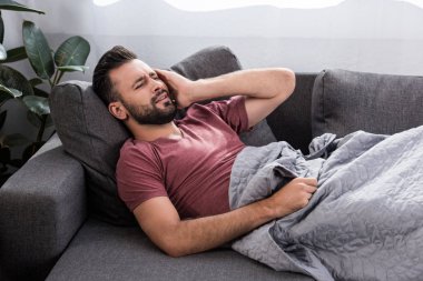 stuffering young man with headache lying on couch clipart