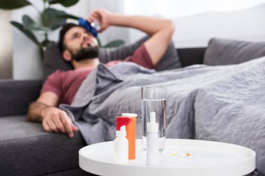 koltukta yalan ve ön plan masaya ilaçlar ile alnına buz tutan hasta genç adam