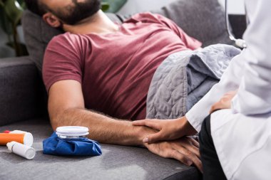 Kırpılan doz ilaç ve buz torbası ile kanepede yatan hasta genç adam