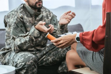 cropped shot of soldier in uniform with ptsd talking to psychiatrist at therapy session while she holding jar of pills clipart