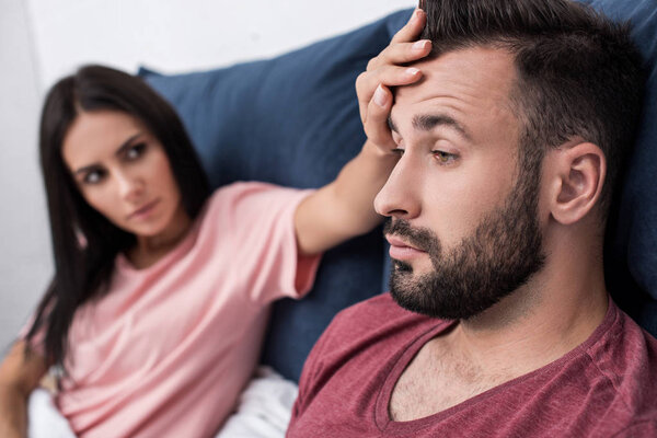 young woman touching forehead of sick husband while sitting in bed