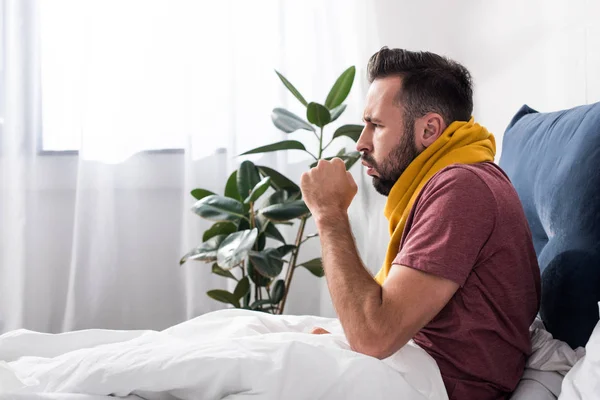 ベッドに座りながら咳を持つ病気の若い男の側面図 — ストック写真