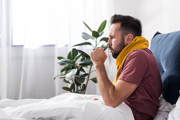side view of sick young man having cough while sitting in bed