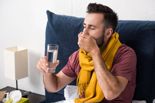 sick young man taking pills while sitting in bed