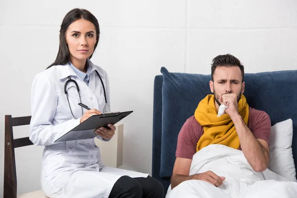 Arzt Schreibt Diagnose Klemmbrett Während Patient Hustet Und Bett Sitzt — Stockfoto