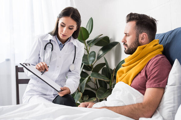 female doctor showing clipboard with documents to patient while lying in bed