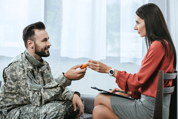psychiatrist giving container of pills to smiling soldier during therapy session
